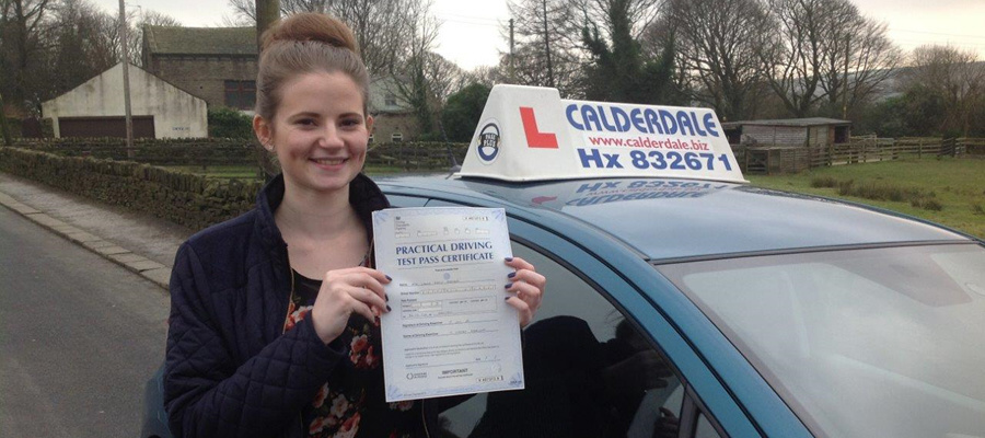 A Calderdale School of Motoring pupil holding her practical driving test pass certificate beside the school car in Halifax